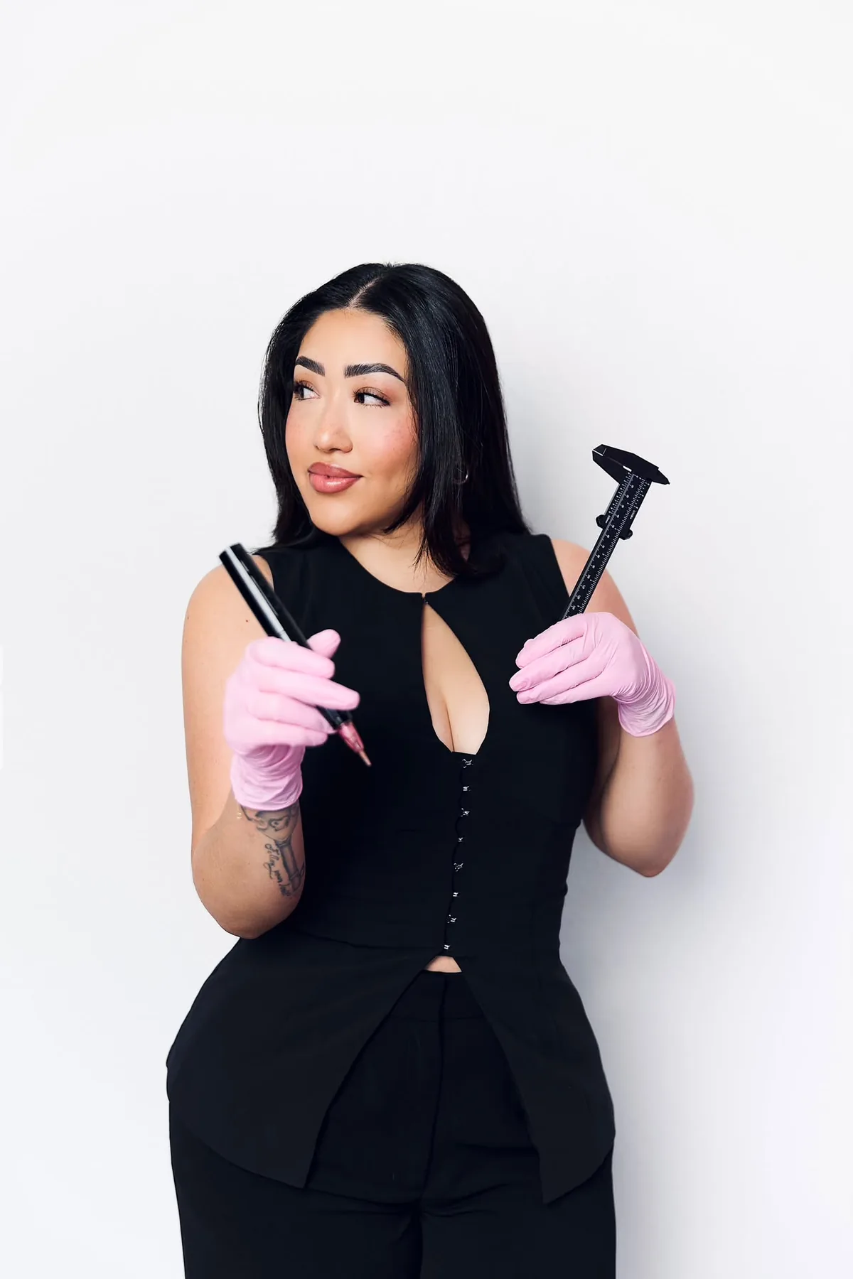 Isis Coheto in pink gloves holding a microblading pen and a brow caliper